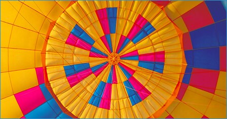 The inside of a colorful hot-air balloon, seen from below, with a circular pattern of yellow, pink and blue panels